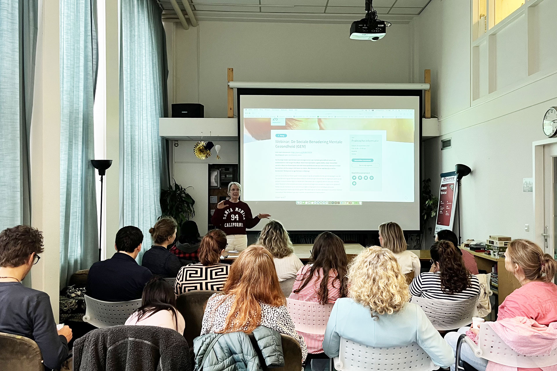 Dineke die met een beamer een presentatie geeft over ontwikkelingen aan een groep deelnemers.
